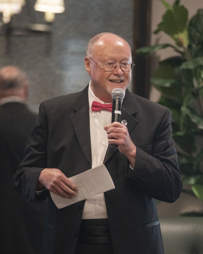 Gentleman speaking into a microphone on stage, holding an envelope. (Photo Credit: Wingate Downs)