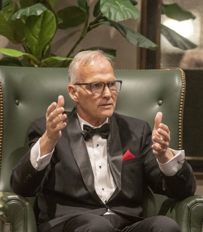 Photo of an gentleman sitting onstage talking about something, holding his hands up in an explanatory gesture. (Photo Credit: Wingate Downs)