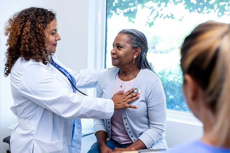 Doctor placing a stethoscope on a woman's chest to hear her heartbeat.