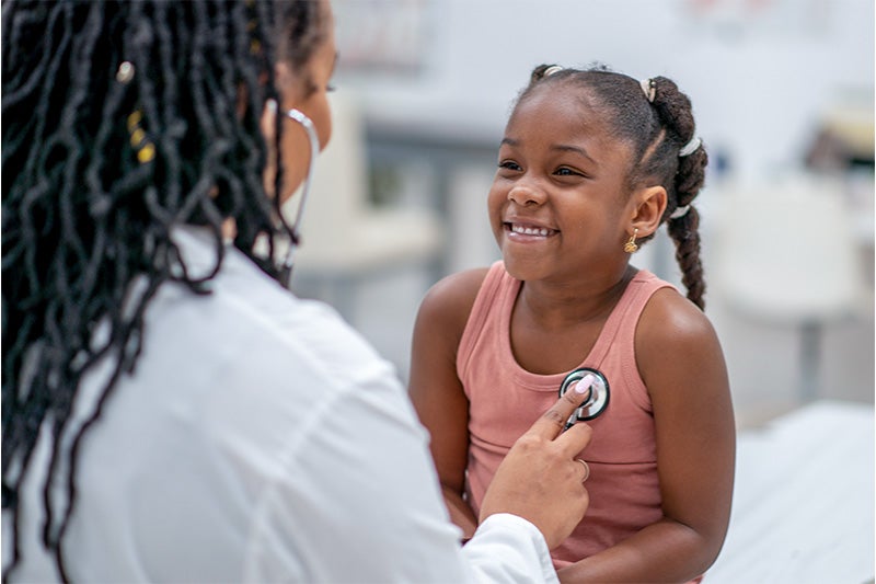 Little girl smiling at a doctor while her heartbeat is checked by a physician.