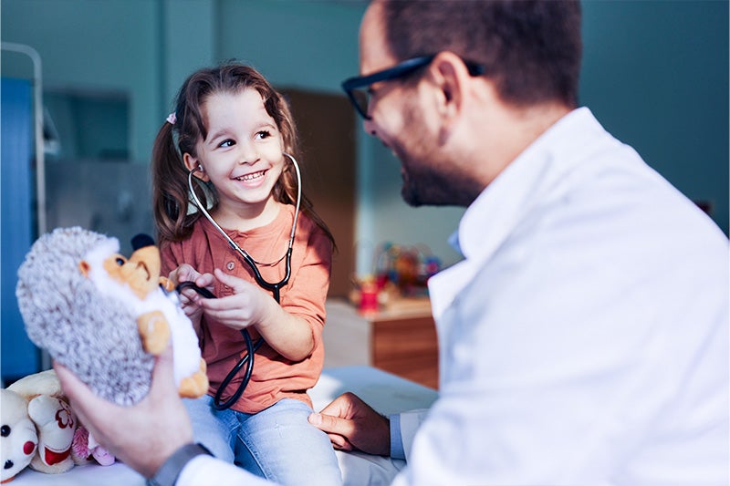 Child and doctor smiling and checking the heartbeat of a teddy bear.