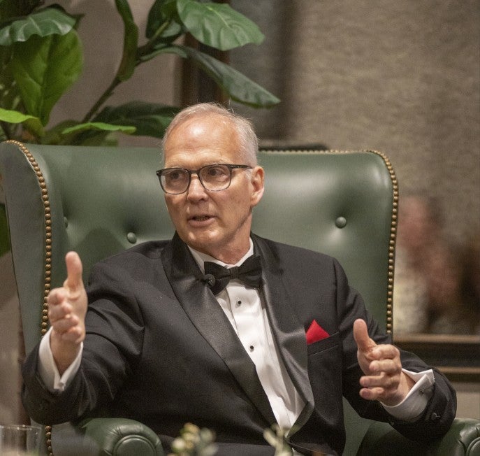 Photo of an gentleman sitting onstage talking about something, holding his hands up in an explanatory gesture. (Photo Credit: Wingate Downs)