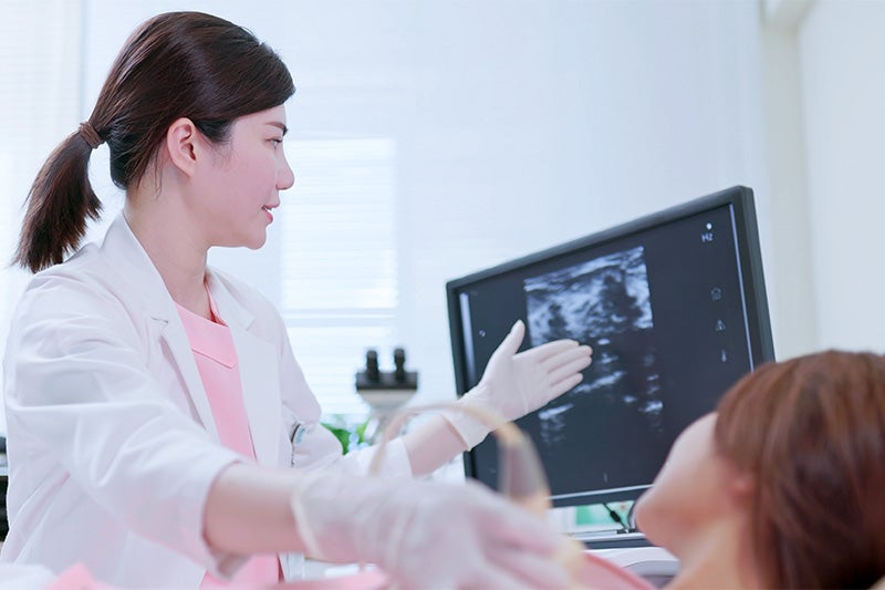 Photo of a woman receiving a breast ultrasound by a physician.