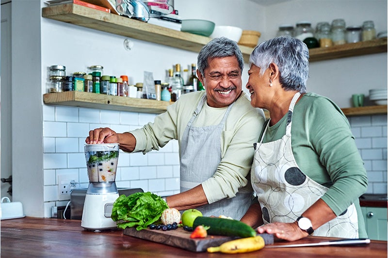 Elderly couple creating a healthy lunch and smiling at one another.
