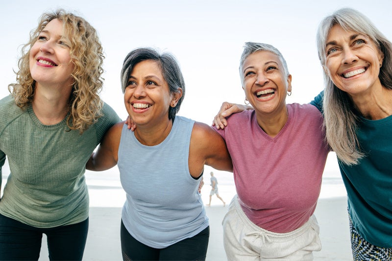 Group of women of perimenopausal age locked arms with one another and smiling at the camera.