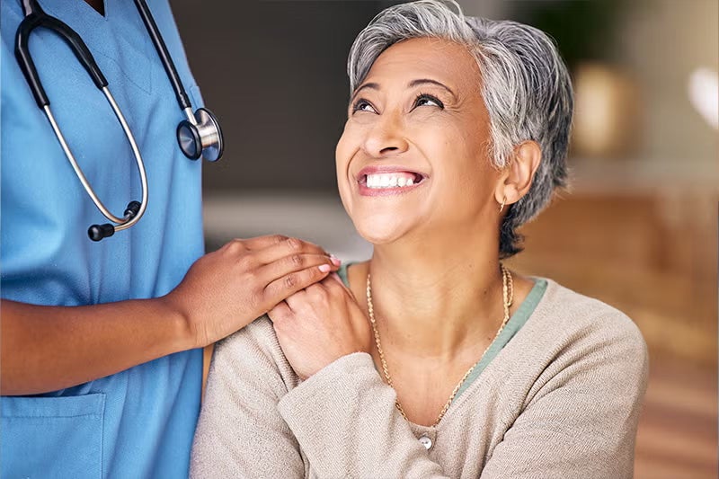 Patient holding a hand placed on her shoulder of a physician who has assisted in her wound care.