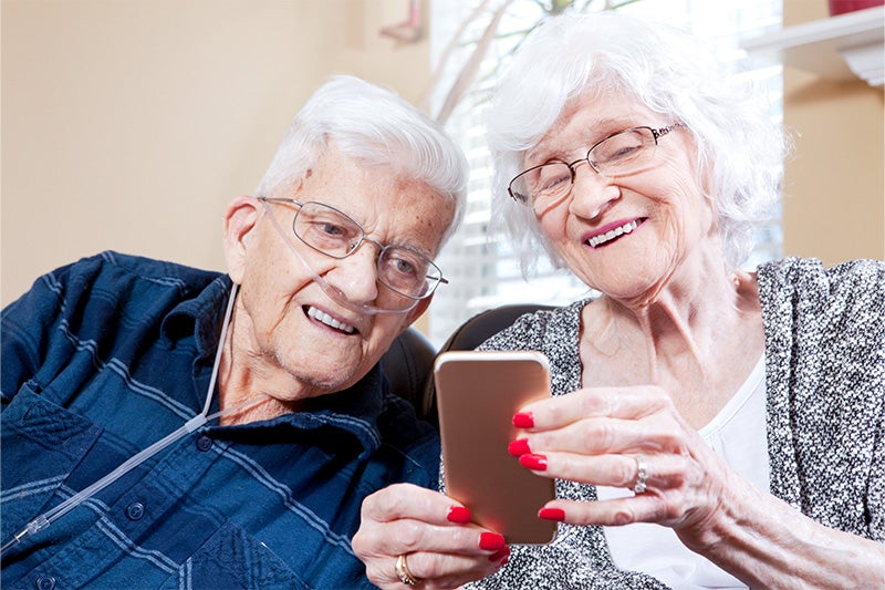 Elderly husband and wife looking at a phone and smiling together.