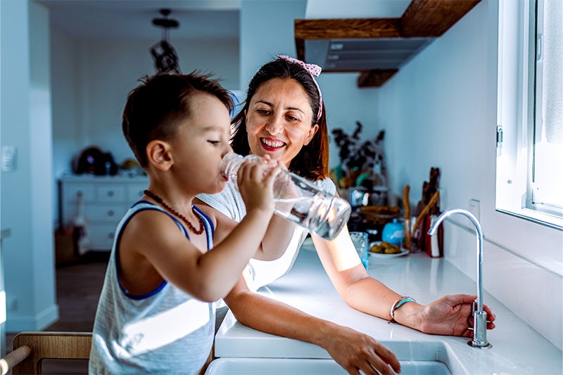 Mother and son drinking water at a fountain, happy after getting his environmental allergies under control.