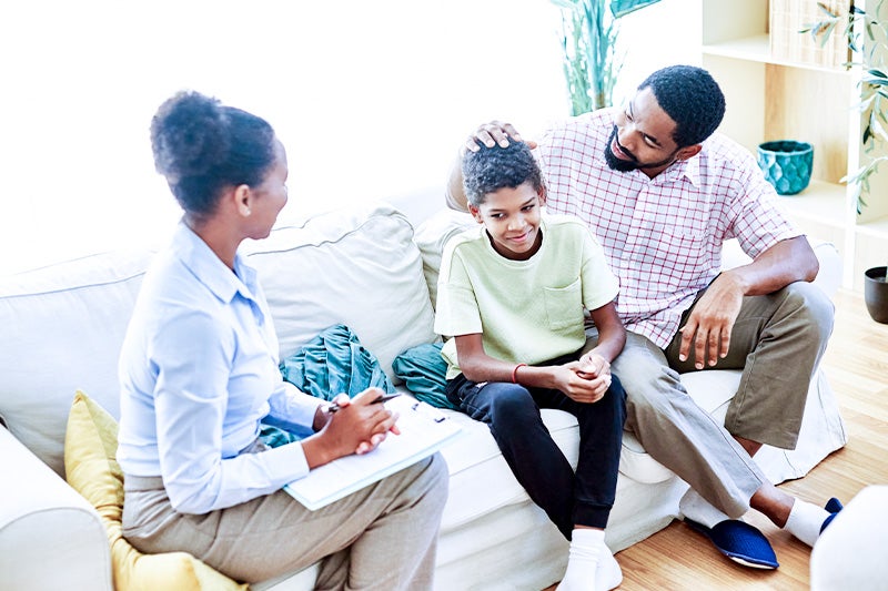 Parents sitting on a couch with a autistic teenager, being supportive.